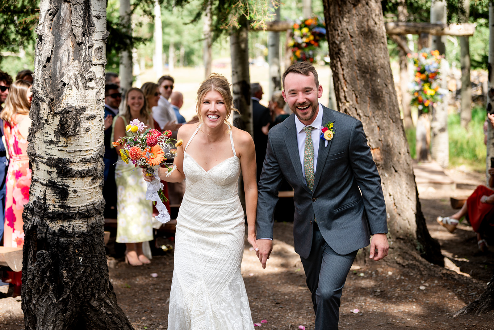 Bride and groom laughing as they walk down the aisle through aspen trees at their Colorado mountain wedding
